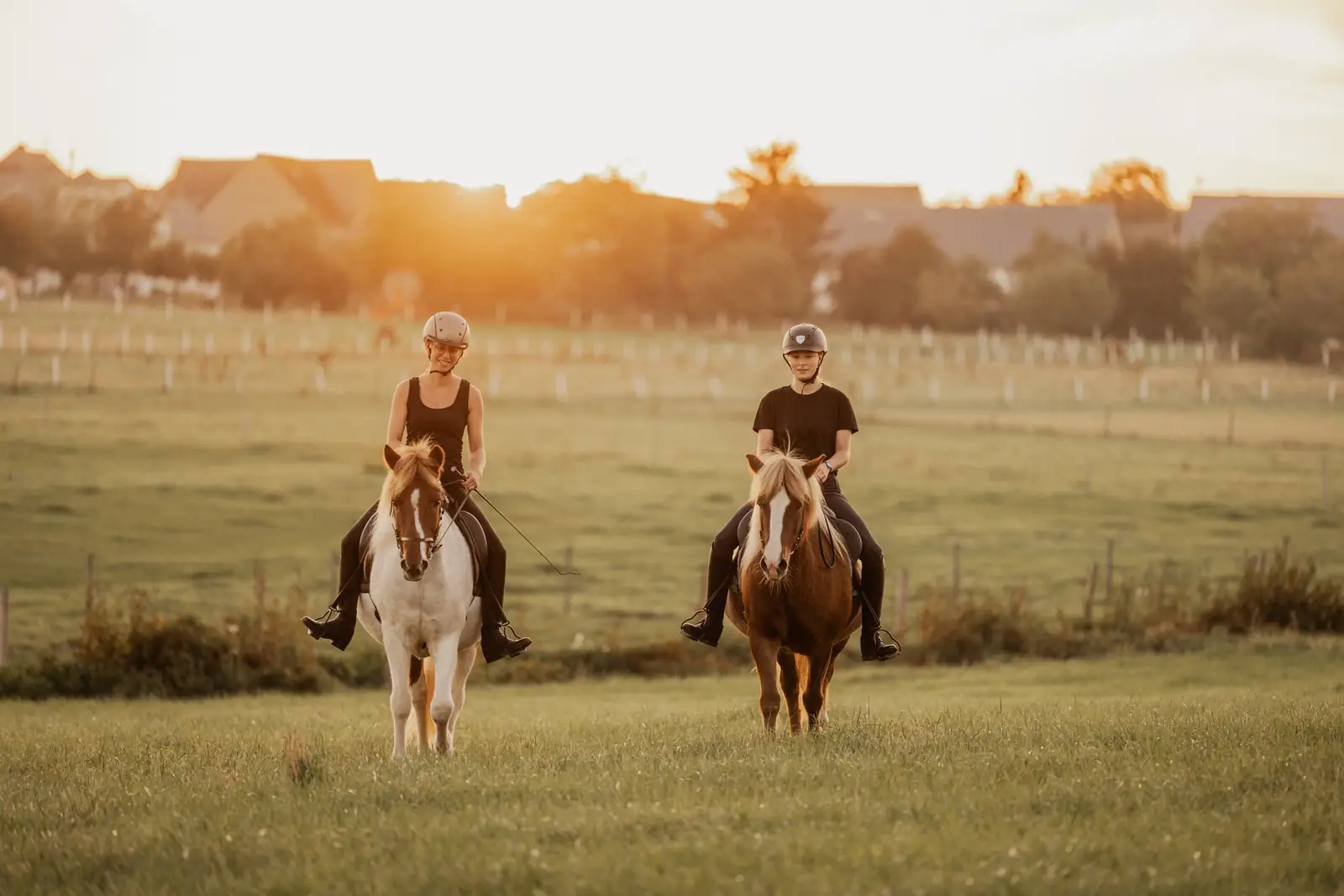 Zwei Reiterinnen auf Ponys vor der untergehenden Sonne über den Feldern bei Hasselbach.