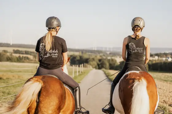 Zwei Reiterinnen auf Ponys von hinten auf einem Feldweg.