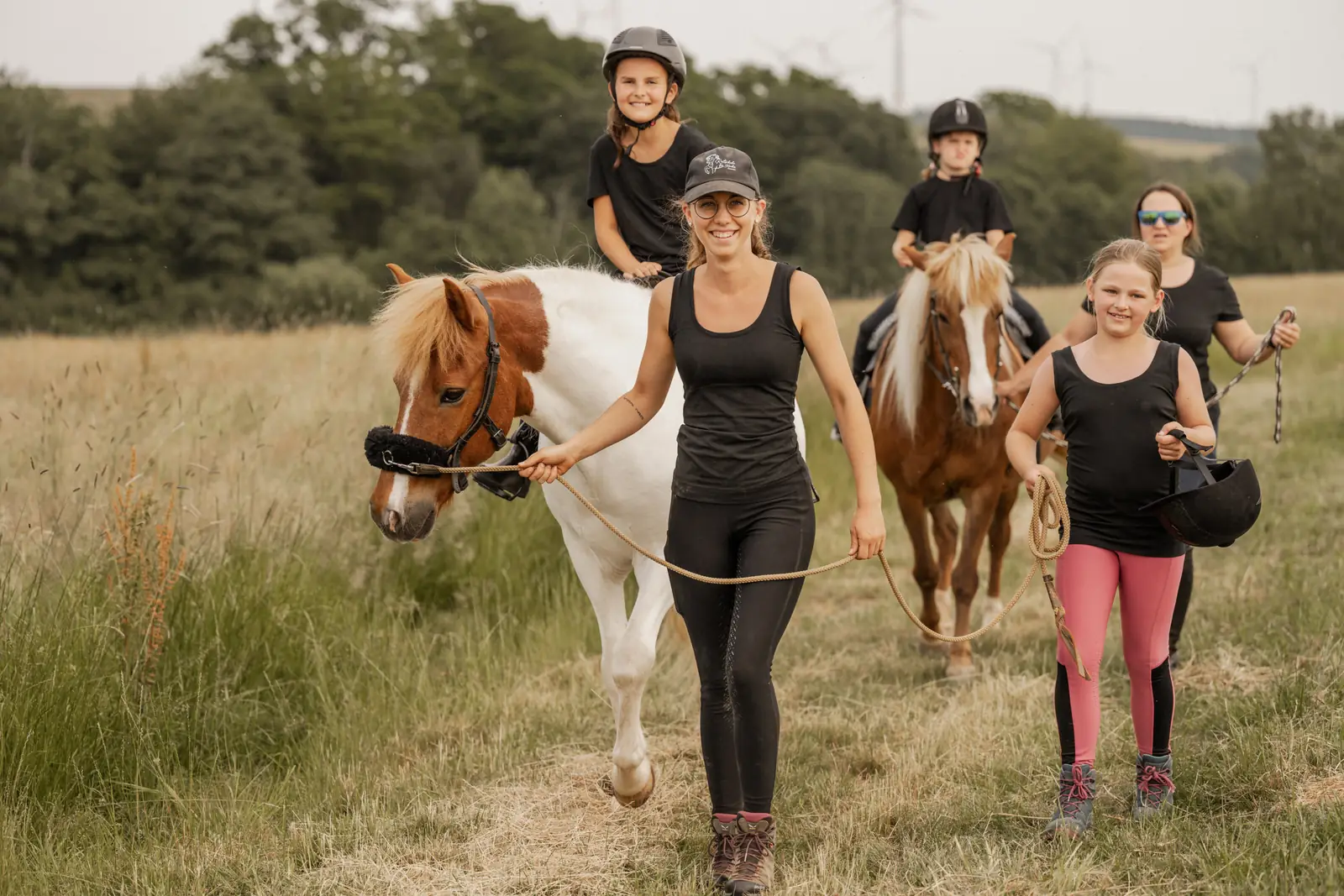 Franziska Falk führt ein Pony durch hohes Gras, drei Kinder folgen mit weiteren Ponys.