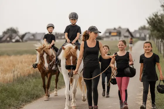 Franziska Falk geht mit Kindern und Ponys über einen Weg am Ortsrand.