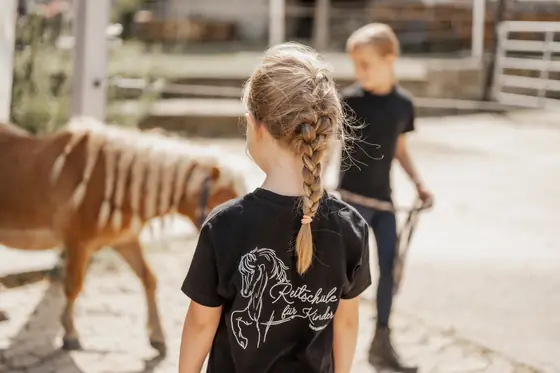 Zwei Mädchen führen ein Pony über den Hof.