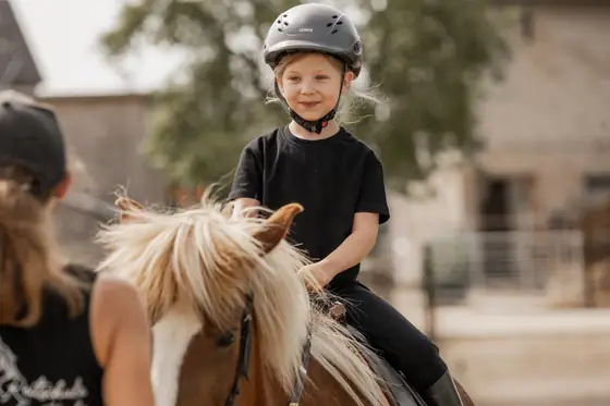 Ein Mädchen sitzt lachend auf einem Pony.